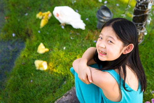 Smiling Asian child sits happily with a group of little yellow ducks.