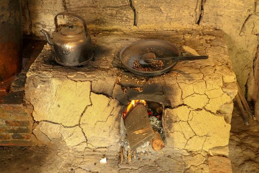 Traditional clay furnace with open fireplace. Primitive way of roasting coffee beans in steel pan at coffee farm in Bali, Indonesia. Simple production of coffee Arabica, Kopi Luwak on coffee factory.
