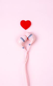 Pink earphones and red heart over pink background. Love to music rhythm concept.