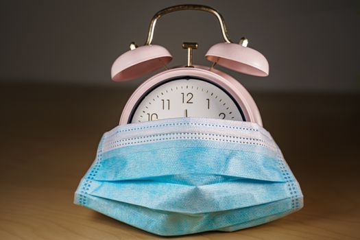Vintage pink alarm clock with a face mask. Time until the end of quarantine, find a vaccine or new normal global concept.