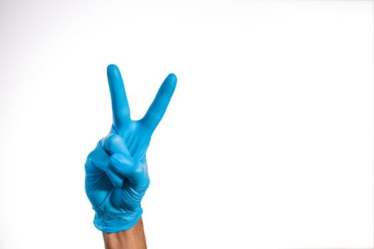 Medical hand with blue glove doing the Victory gesture, symbolizing the fight and victory over diseases such as COVID-19 by coronavirus