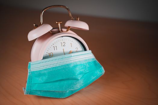 Vintage pink alarm clock with a face mask. Time until the end of quarantine, find a vaccine or new normal global concept.