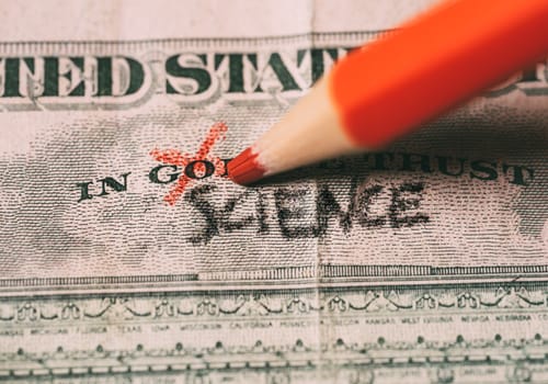 hand crossing out the word God for science on on a US dollar bill. Suitable for atheism, coronavirus vaccine or science as new relligion concepts.