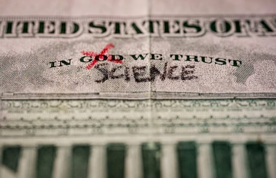 word God crossed out and replaced by science on a US dollar bill. Suitable for atheism, coronavirus vaccine or science as new relligion concepts.