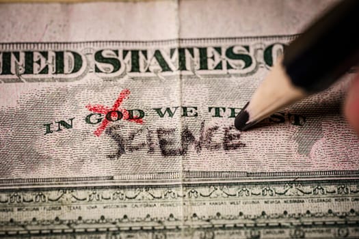 hand replacing the word god for science on on a US dollar bill. Suitable for science research, coronavirus vaccine or science as new relligion concepts.
