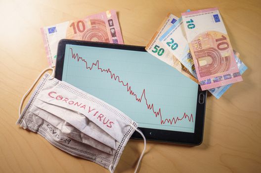 Euro bills and respirator mask with the word coronavirus over a a tablet with stock market down chart on screen. Global stock markets financial crisis and crash caused by the coronavirus outbreak