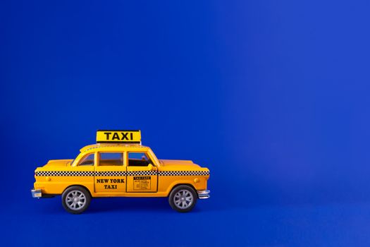 Model of yellow retro New York city taxi cab against a blue background. Complementary colors and copy space available