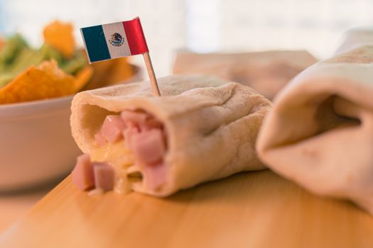 Close up of a hot fresh burrito with the mexican flag and nachos with guacamole cream. The first Thursday in April of every year is the National Burrito day