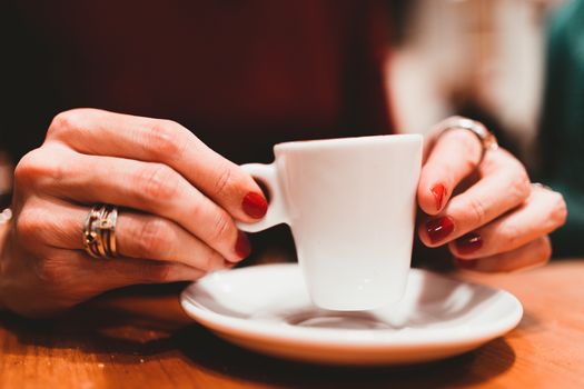 Woman holding in hands cup of coffee on wooden table in cafe. Close up.