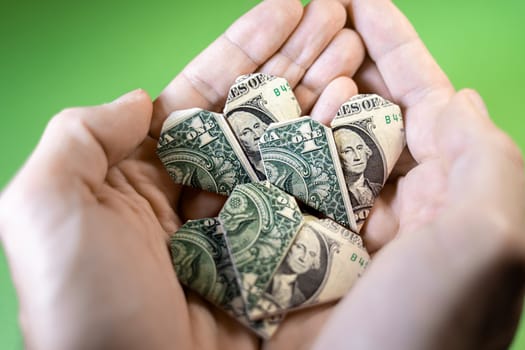 Hands holding one Dollar origami hearts on a paper background. Paper craft, suitable for greed, business, richness or money love concepts with available copy space.