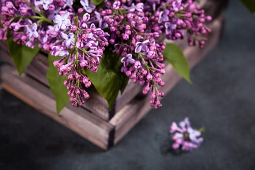 Purple lilac flowers bouquet on wooden box on black concrete background. Stylish floral greeting card. Happy mothers day.
