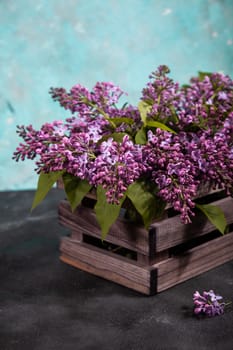Purple lilac flowers bouquet on wooden box on black concrete background. Stylish floral greeting card. Happy mothers day.