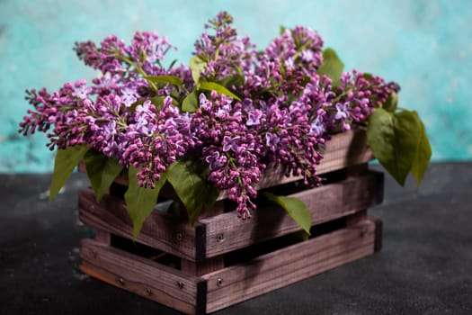 Purple lilac flowers bouquet on wooden box on black concrete background. Stylish floral greeting card. Happy mothers day.