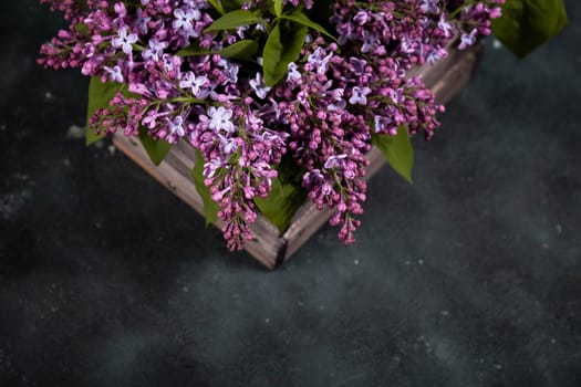 Purple lilac flowers bouquet on wooden box on black concrete background. Stylish floral greeting card. Happy mothers day.