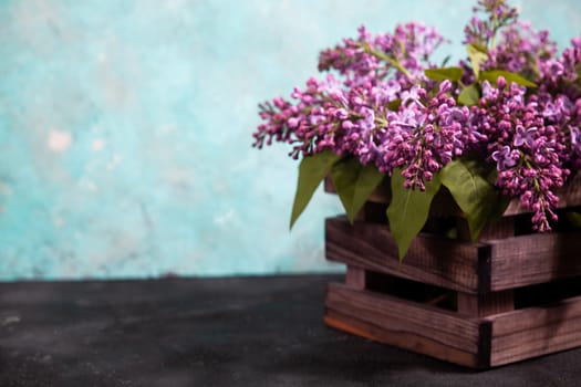 Purple lilac flowers bouquet on wooden box on black concrete background. Stylish floral greeting card. Happy mothers day.