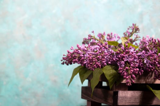 Purple lilac flowers bouquet on wooden box on black concrete background. Stylish floral greeting card. Happy mothers day.