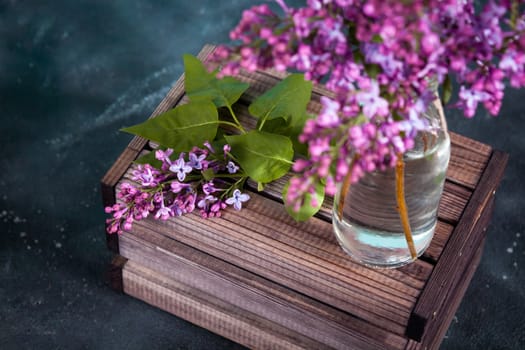 Purple lilac flowers bouquet on wooden box on black concrete background. Stylish floral greeting card. Happy mothers day.
