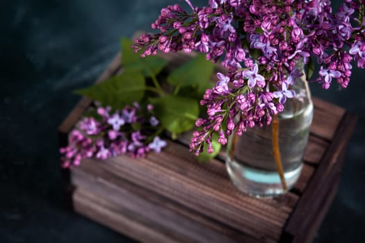 Purple lilac flowers bouquet on wooden box on black concrete background. Stylish floral greeting card. Happy mothers day.