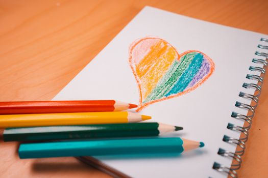 Heart with the colors of the LGTBI or GLBT flag on a blank notebook with rainbow pens. Copy space to add some text or graphics