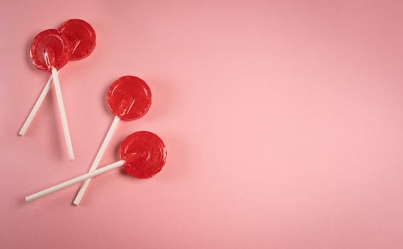 Round shaped red sweet tasty lollipops on pink pastel background. St. Valentine's day. Copy space.