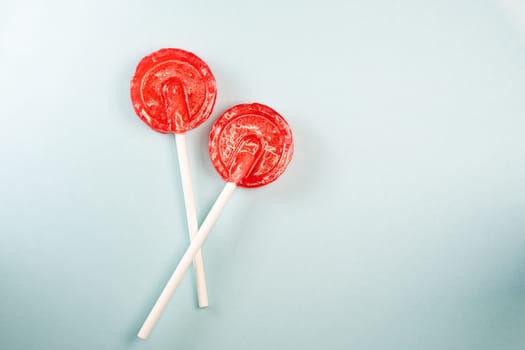Round shaped red sweet tasty lollipops on blue pastel background. St. Valentine's day. Copy space.
