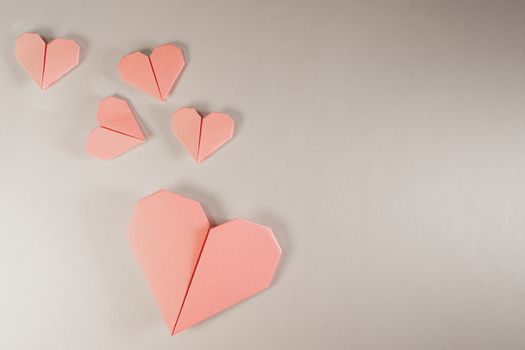 Pink origami hearts on a paper background. Paper craft, suitable for love, Valentine Day, romance and wedding concepts with copy space available.