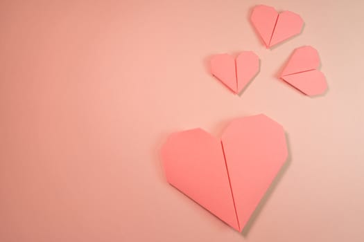 Pink origami hearts on a pink background. Paper craft, suitable for love, Valentine Day, romance and wedding concepts with copy space available.