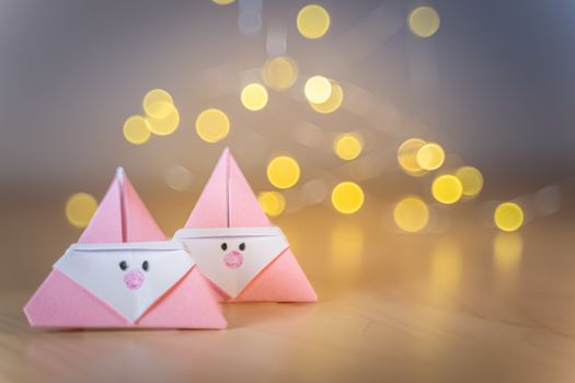 Origami Xmas scene with two pink Santa claus in paper craft and bokeh lights on the background