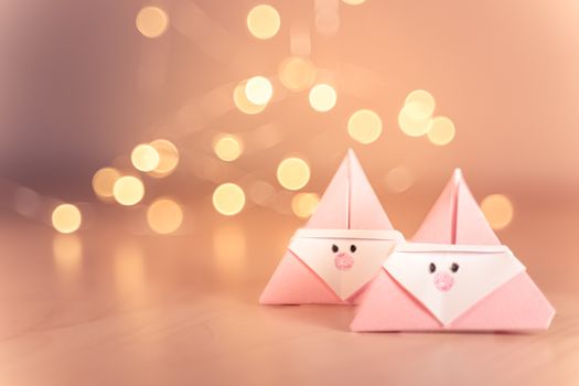 Origami Xmas scene with two pink Santa claus in paper craft and bokeh lights on the background. Sepia tone