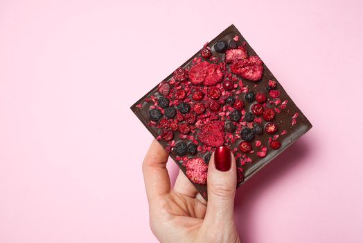 hand holding homemade chocolate with berries on pink background