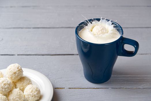 coconut cookies fell into a blue mug of milk. splashes of milk in a mug caused by a drop of coconut truffle