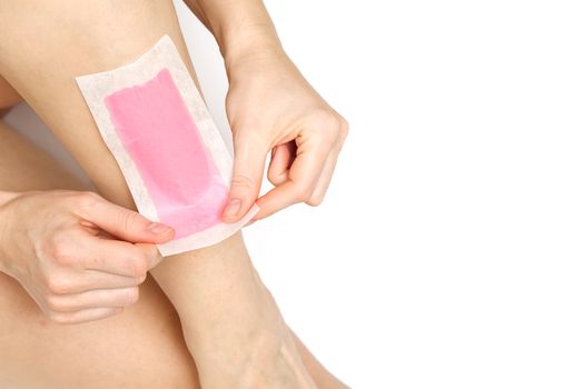 Beautiful woman doing depilation for her legs with waxing, isolated on white. Woman using pink wax strips.