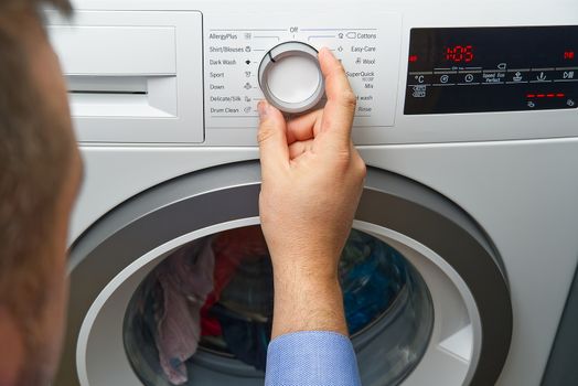 The man sets the program and turns on the washing machine. Close-up Of Person Hand Pressing Button Of Washing Machine For Clothes Laundry.