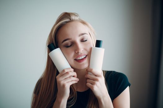 Pretty young woman hold two bottle with empty space. Shampoo and conditioner.
