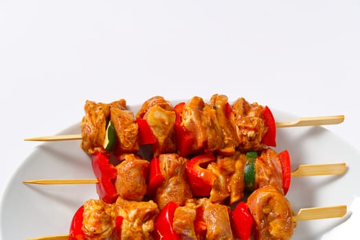 raw marinated meat on wooden skewers, pork, chicken, beef in white plate on white background