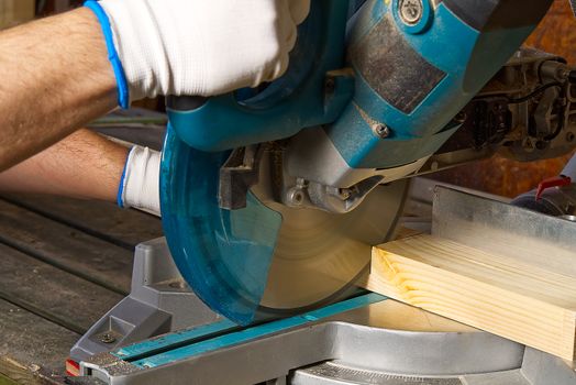 Closeup of professional cabinet makers working with electric circular saw at woodworking workshop. Skilled carpenter cutting wooden board with circular saw. Wood material production. Lumber factory.