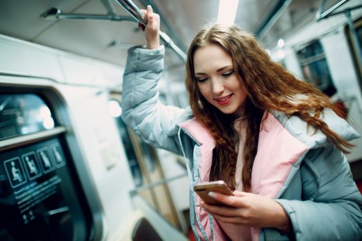 Young woman smiling with mobile phone in subway. Wi fi in metro concept.