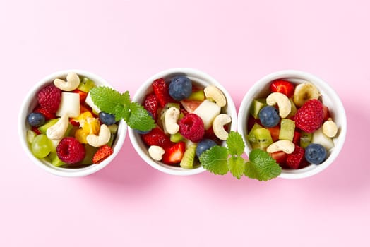 Three bowls with fruit salad. Fresh fruit salad on white bowl. Mixed fruit in white bowl healthy food style. Useful fruit salad of fresh fruits and berries on pink background.