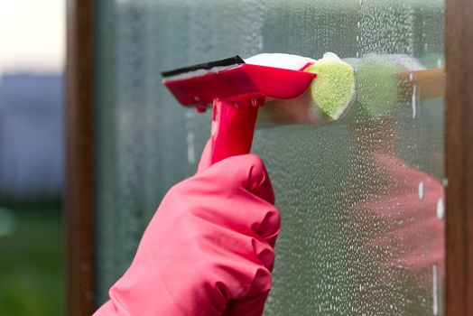 window cleaning. A woman in pink rubber gloves washes a window in a house. Happy Woman In Gloves Cleaning Window Concept for home cleaning services.