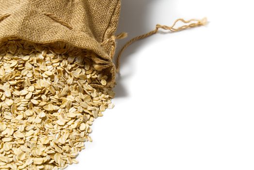 oatmeal spills out of a linen bag. dry natural oat flakes. Natural linen eco bag with oatmeal flakes on white background.