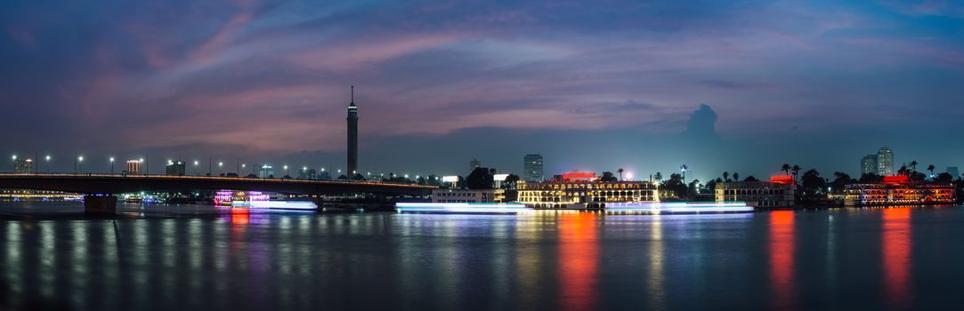 Panoramic of Cairo city center at night, long exposure with light trails of moving boats on the Nile river.