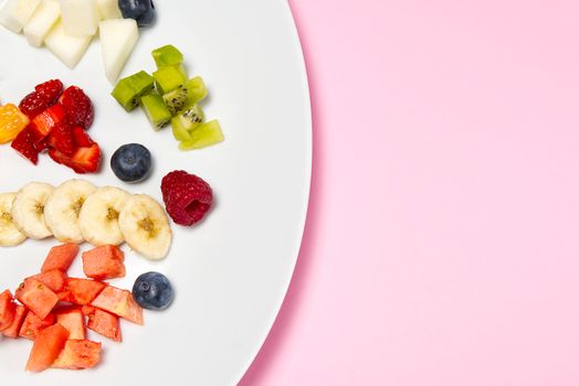 Fresh fruit salad on white plate. Mixed fruit in white plate healthy food style. Useful fruit salad of fresh fruits and berries on pink background.