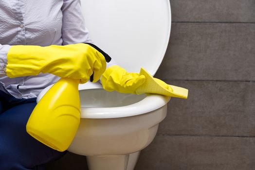 Woman in yellow rubber gloves cleaning toilet with pink cloth
