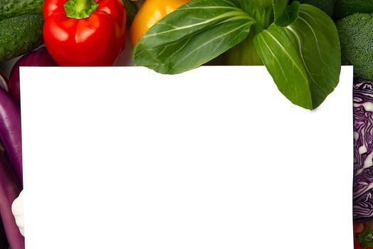 Blank piece of paper is lying on a vegetables layout with different kinds of vegetables. Mock up . Food background border frame of colorful fresh vegetables. Domestic kitchen. Vegetarian food