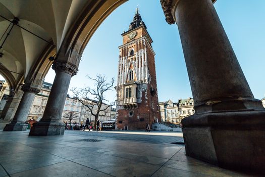 Krakow, Poland - December 30, 2017: Wide angle view of the Town Hall Tower, seen through the columns of the Cloth Hall located on the main market square in the old town of Krakow.