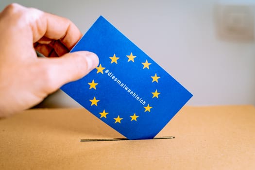 Election in European Union - voting at the ballot box. Hand putting in the ballot box an EU flag vote with thistimeimvoting in german, diesmalwaehleich, hashtag campaign