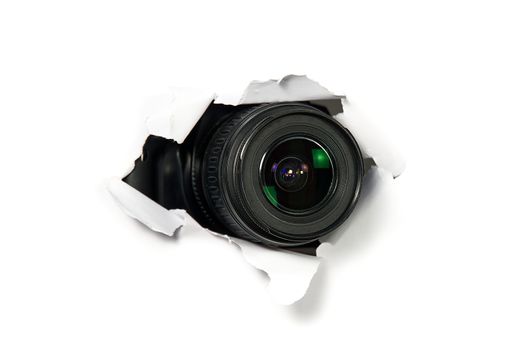 black camera with a telephoto lens that looks out through a hole in white paper. Concept of paparazzi, espionage, yellow press. camera lens looking through hole in wall