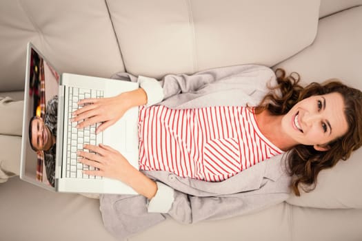 Woman using laptop while lying on sofa at home against smiling man smiling at christmas