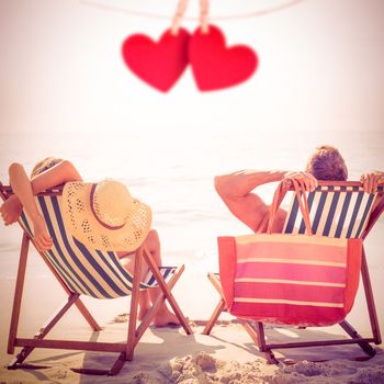 Couple relaxing on the beach against hearts hanging on a line