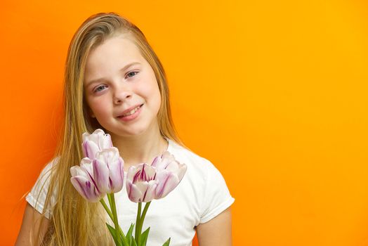 smiling young handsome girl on an orange background with tulips in hands. Children happiness